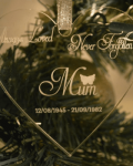 Always Loved Never Forgotten Christmas Ornament . Shows a clear acrylic glass like heart hanging from a silver glittery ribbon with the words "Always Loved Never Forgotten Mum 12.08.1945 - 21.09.1982" in white writing and a picture of a white angel wings over the word Mum